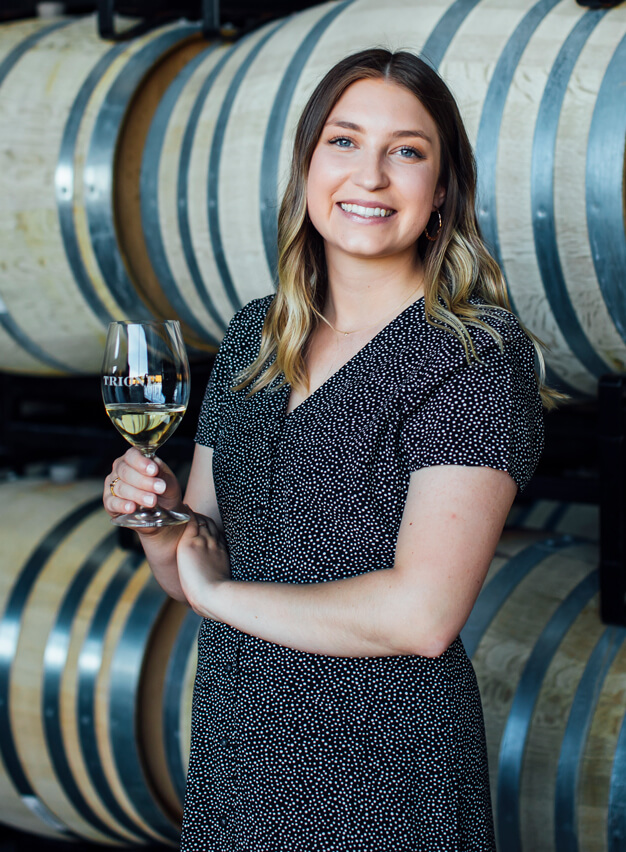 Young woman standing in front of barrels with a glass of wine