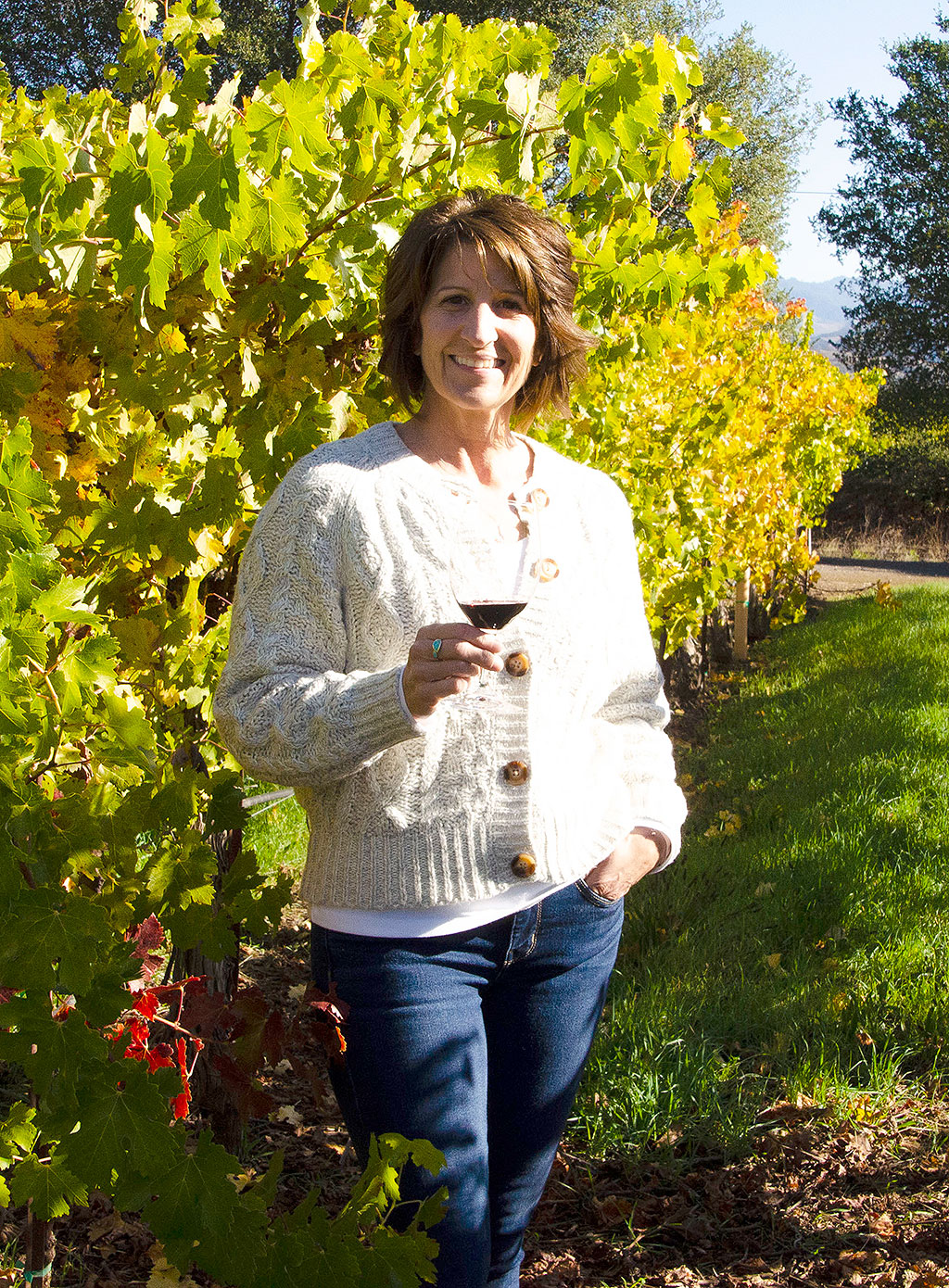 Woman holding a glass or red wine standing in a vineyard row