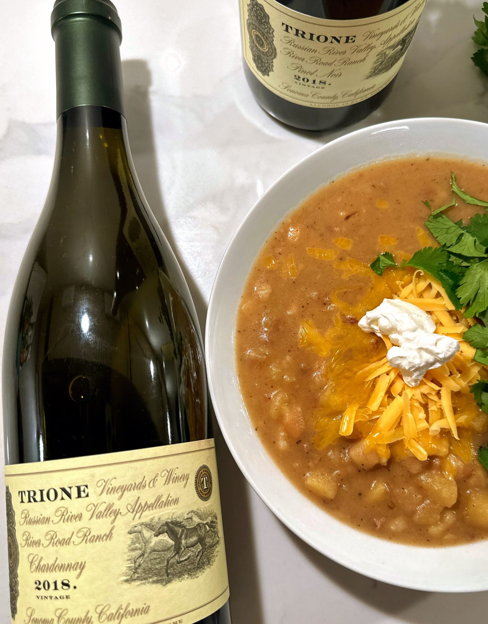 Two bottles of wine with a bowl of soup that has cheese, sour cram and cilantro as garnish.