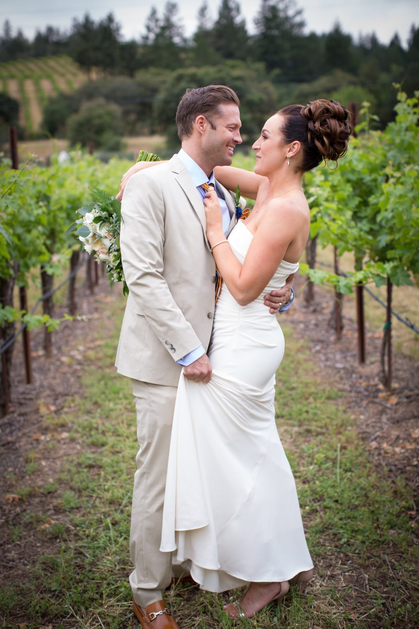 a bride and groom embrace in the vineyards