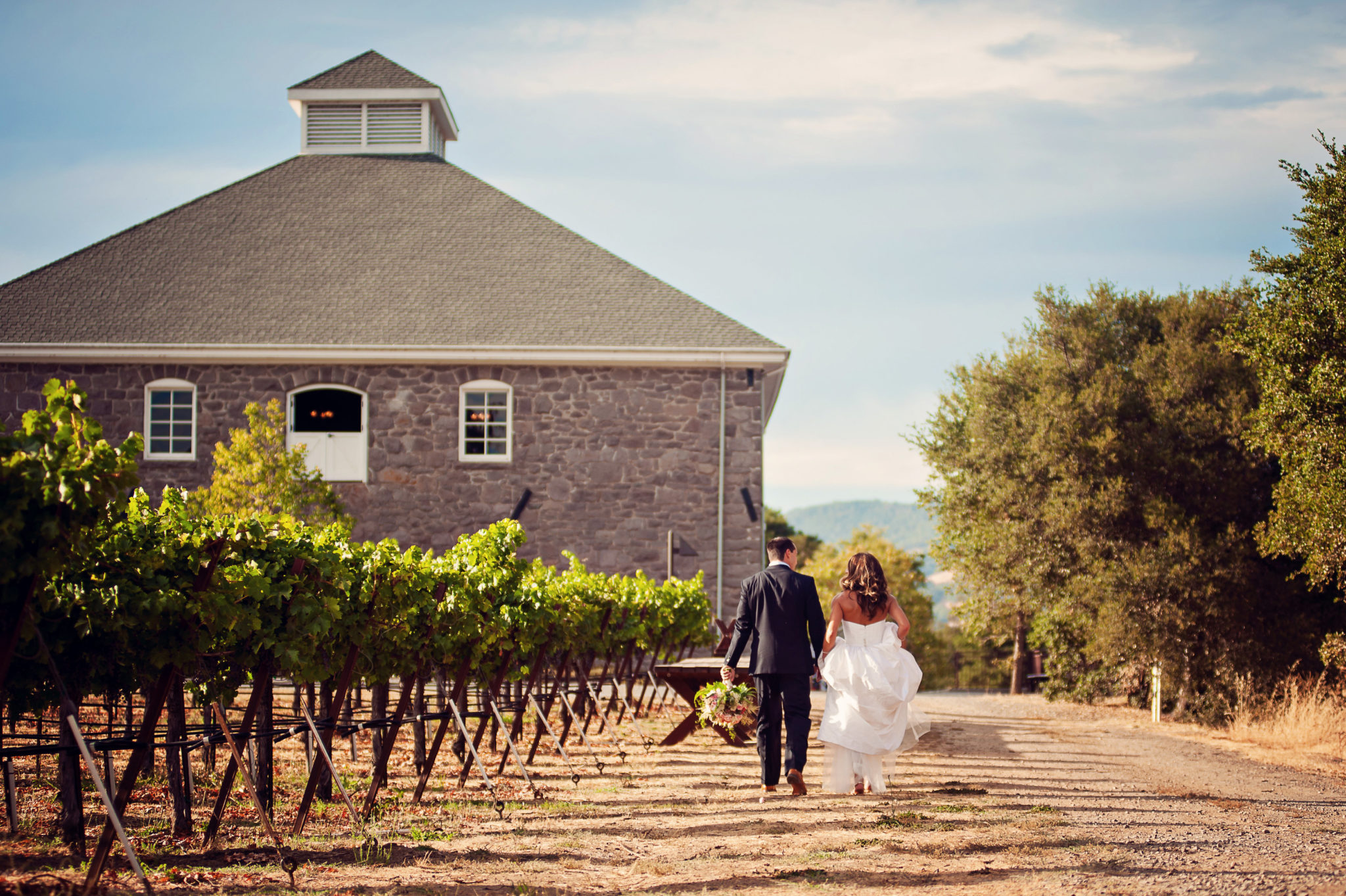 two newlyweds take a stroll through the vineyars at Trione by the o;ld stone building
